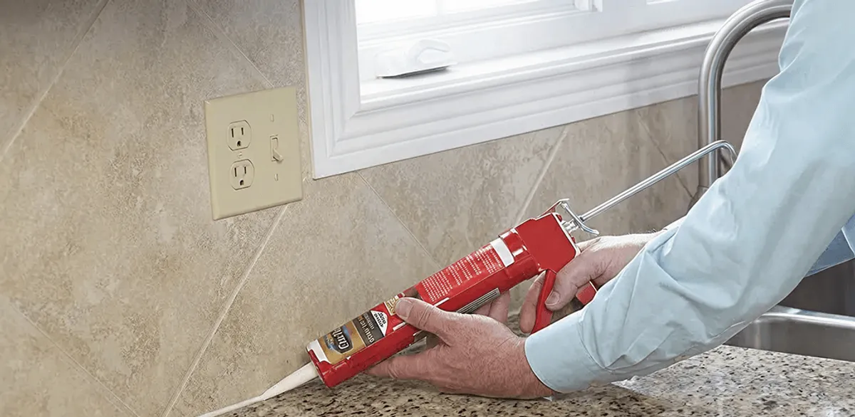 Handyman applying caulk along a kitchen backsplash and countertop seam in Atlanta, GA
